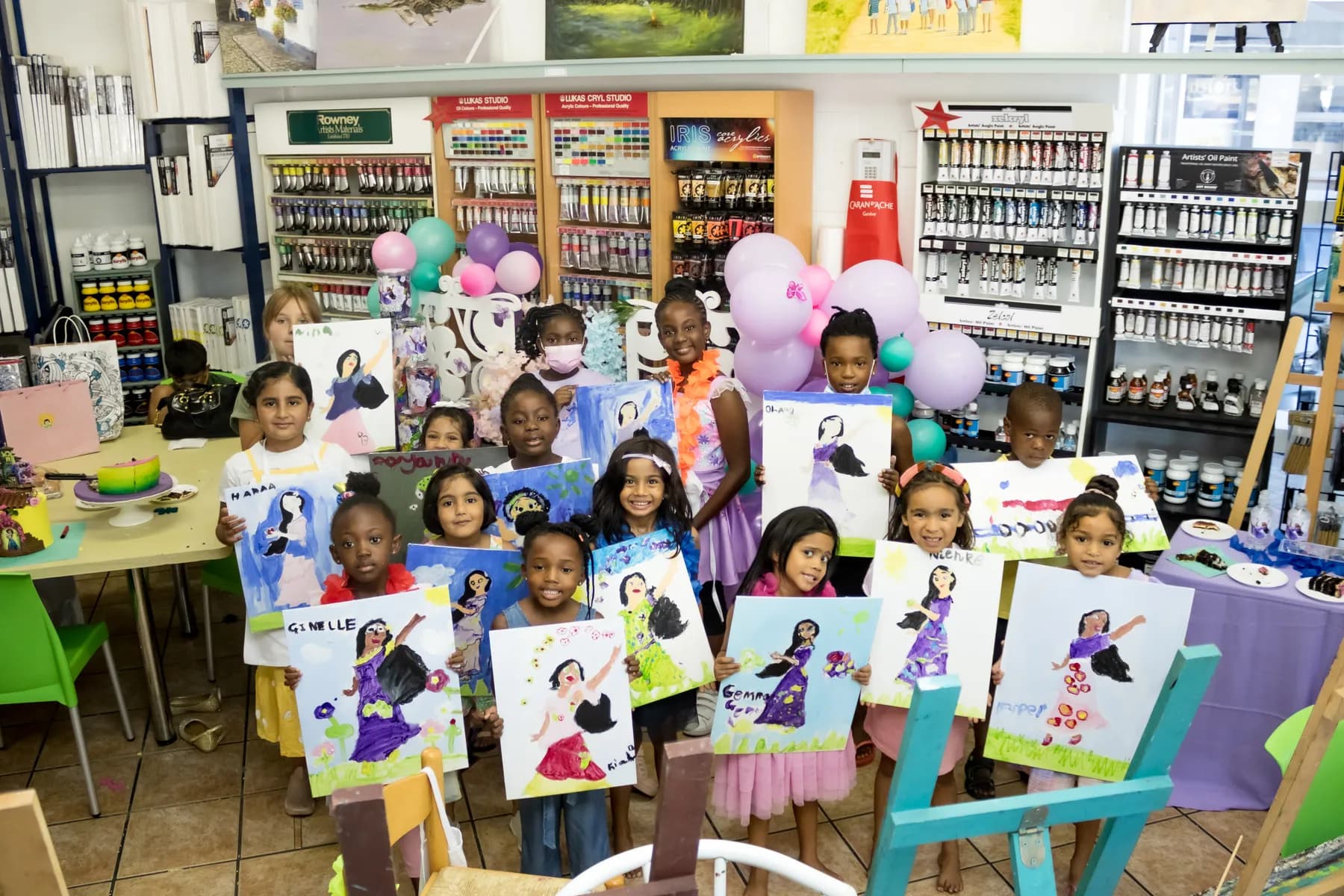 A group of young students holding up their finished painted portraits in the art studio