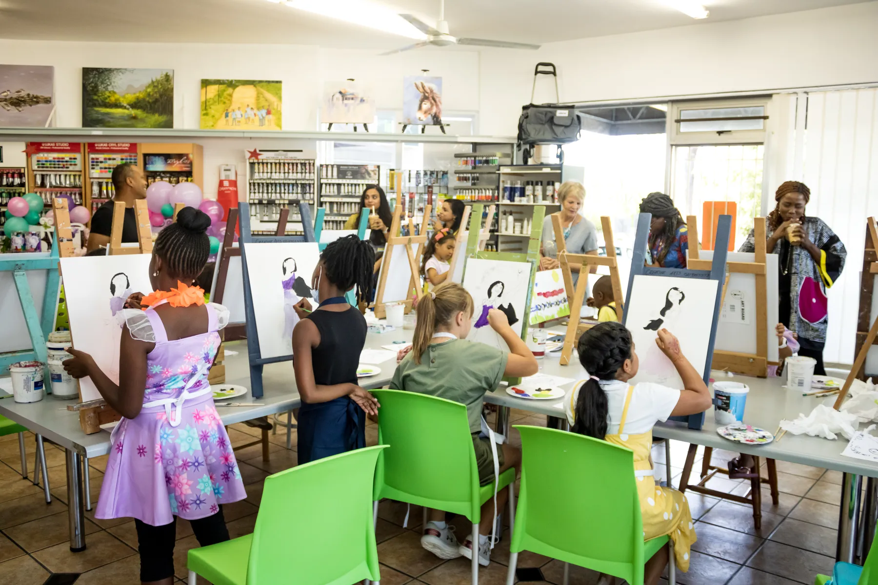 A full class of children painting at white easels in Kay's bright, supply-lined art studio
